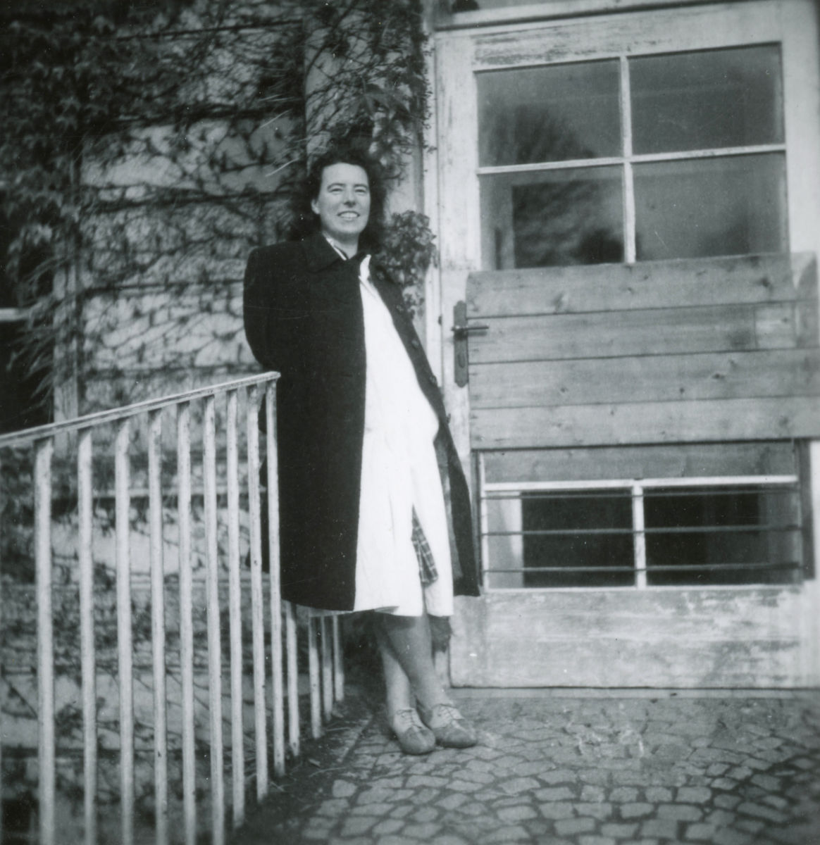 Erika Pallua in Mantel und Arztkittel vor dem Sanatorium Wien-Gersthof