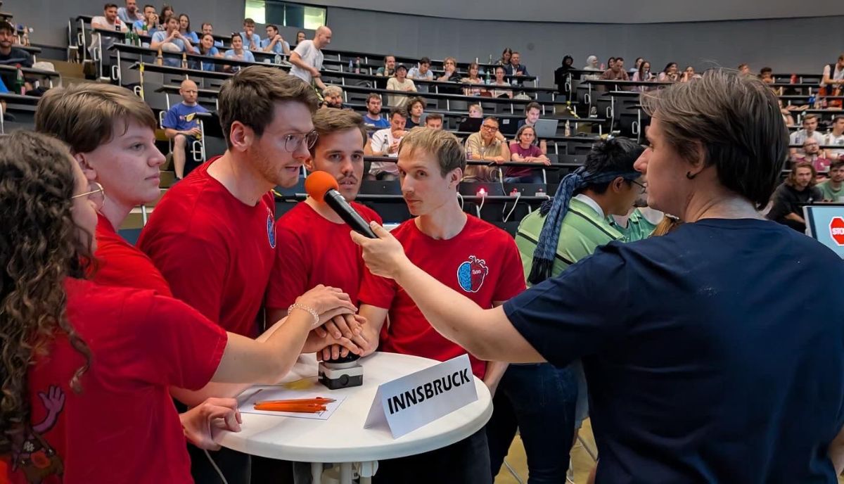 Johannes Miehling spricht bei einer Raterunde ins Mikrofon, umringt von seinen TeamkollegInnen