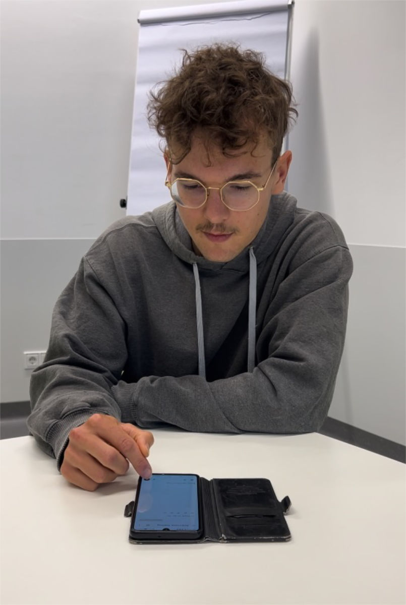 Ben Hofbauer tippt auf sein Smartphone, das vor ihm am Schreibtisch liegt.