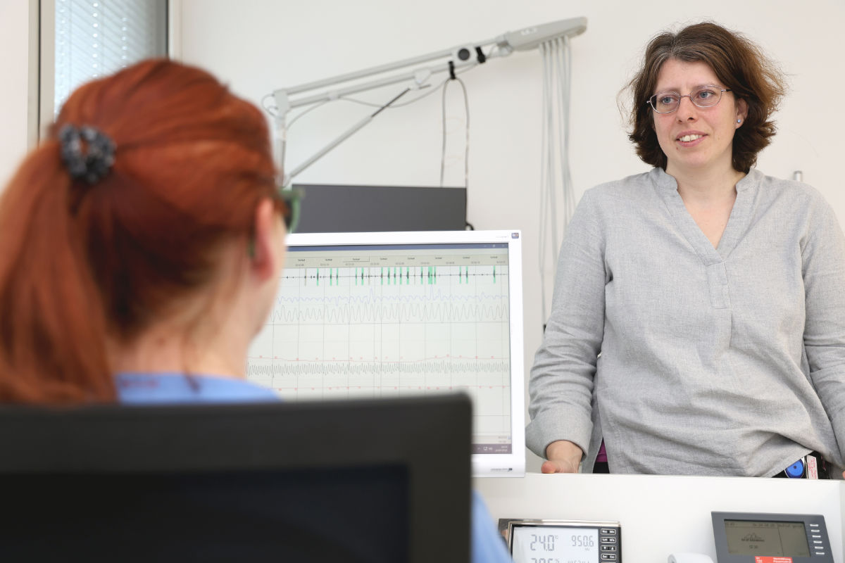 Birigt Sailer im Gespräch mit einer Person am Computer, die man nur von hinten sieht.