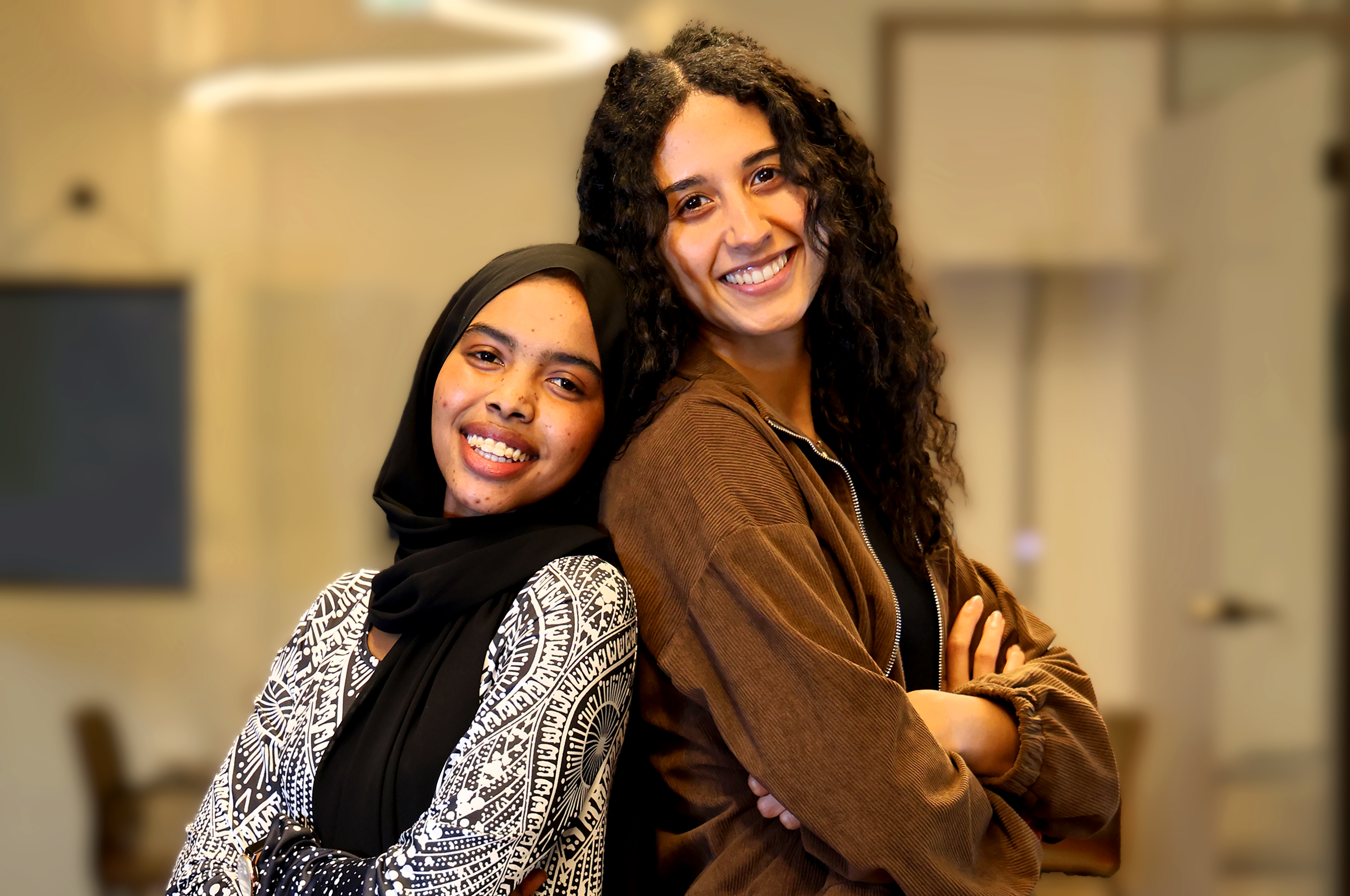 Marwa und Hager blicken, Rücken und Rücken stehend und mit verschränkten Armen, lächelnd in die Kamera