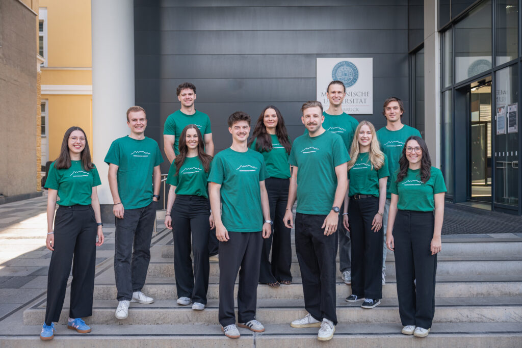Gruppenfotos mit 11 Studierenden in T-Shirts mit dem Logo des Trainingszentrum vor dem Med-Uni-Innsbruck-Gebäude